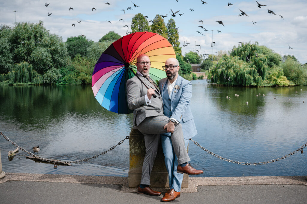 Dani and Stu next to the river in Derby. Stu is holding an umbrella recreating a Doctor Who publicity photo from 1986 whilst Dani holds his leg. Photo taken by Birmingham Gay Wedding Photographer Paul Phipps-Williams