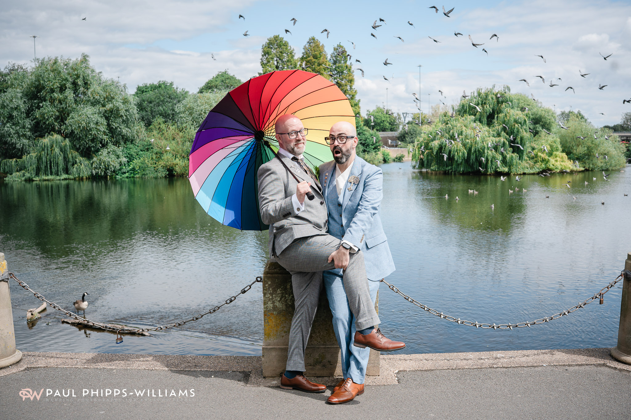 Two grooms with a rainbow umbrella next to the river in Derby
