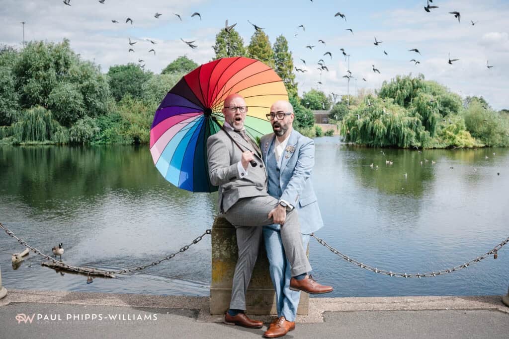 Two grooms with a rainbow umbrella next to the river in Derby