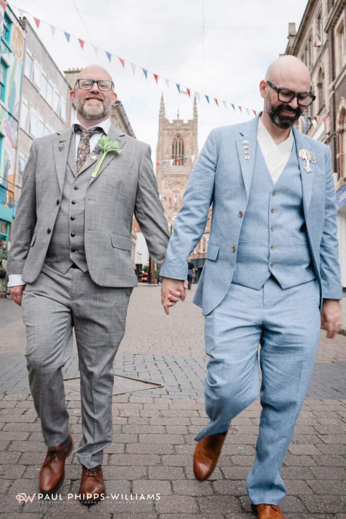 Two grooms walk hand in hand in front of the church in Derby Town Centre