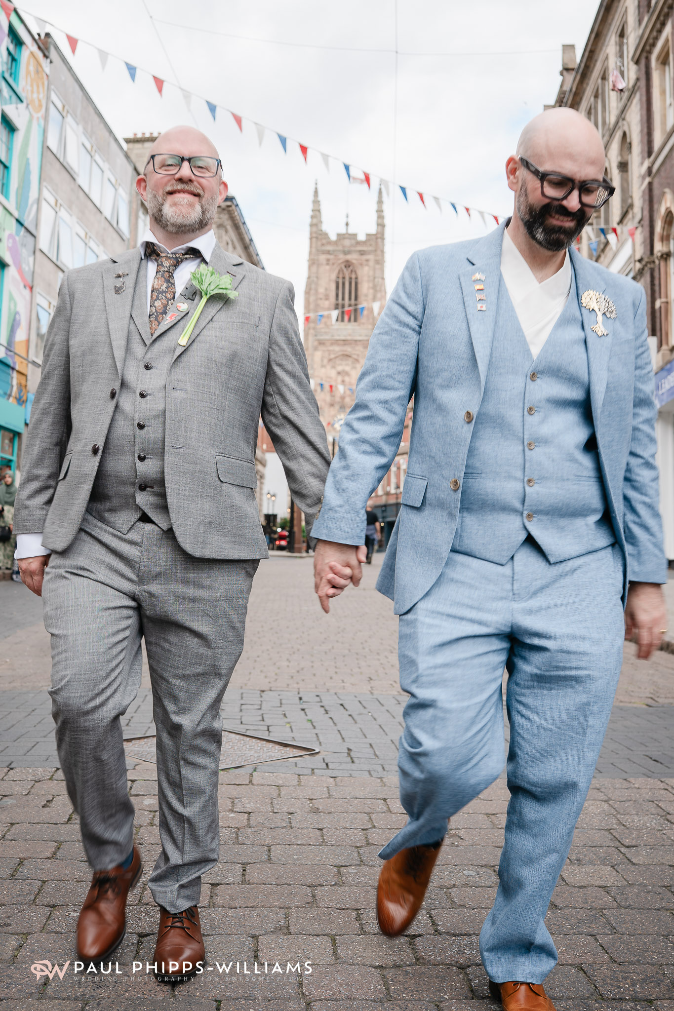 Two grooms walk hand in hand in front of the church in Derby Town Centre