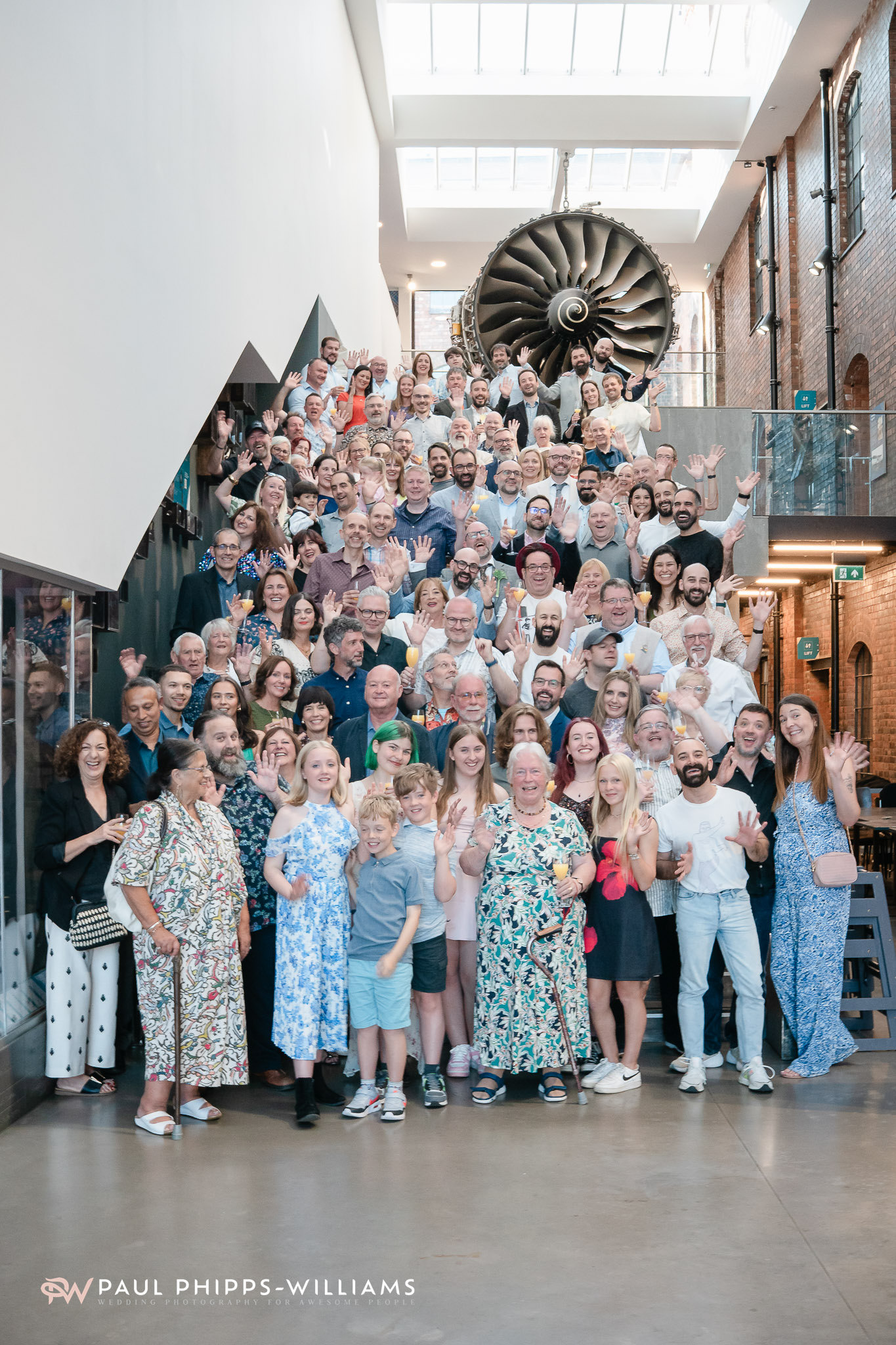 Over a hundred wedding guests do jazz hands on the staircase at the Museum of Making