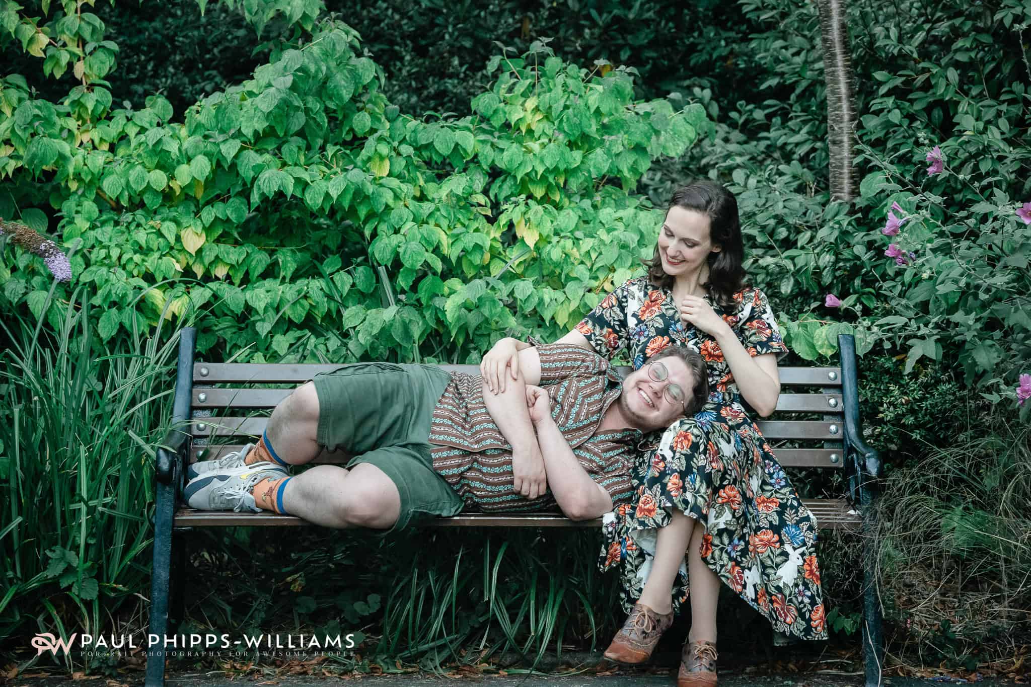 Relaxed couple sitting on a garden bench surrounded by vibrant green plants and foliage.