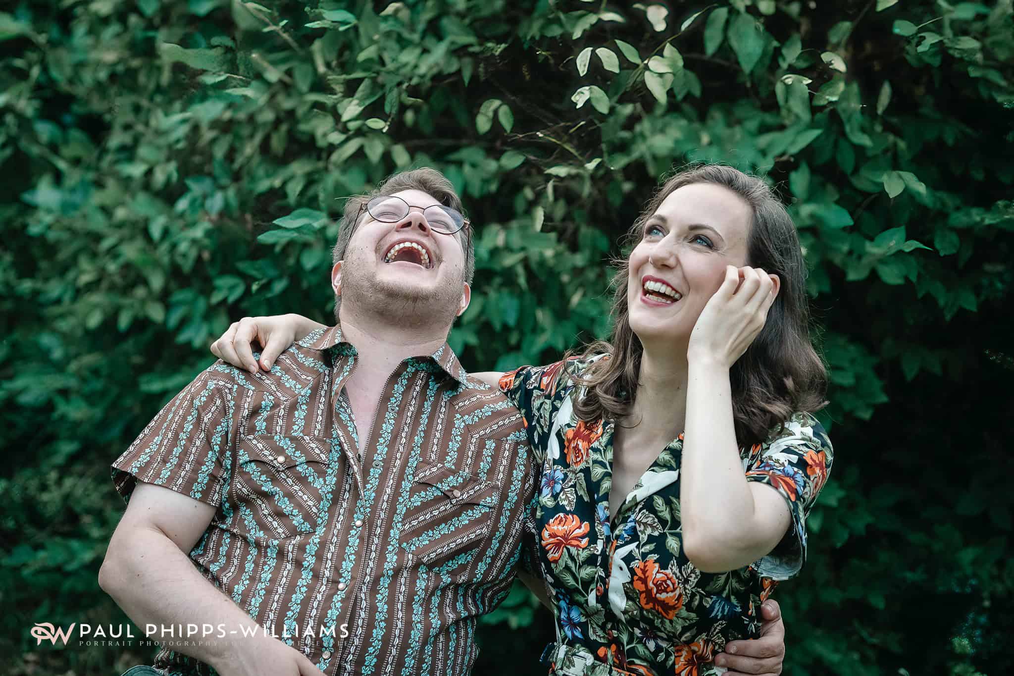 Happy couple laughing outdoors in lush greenery.