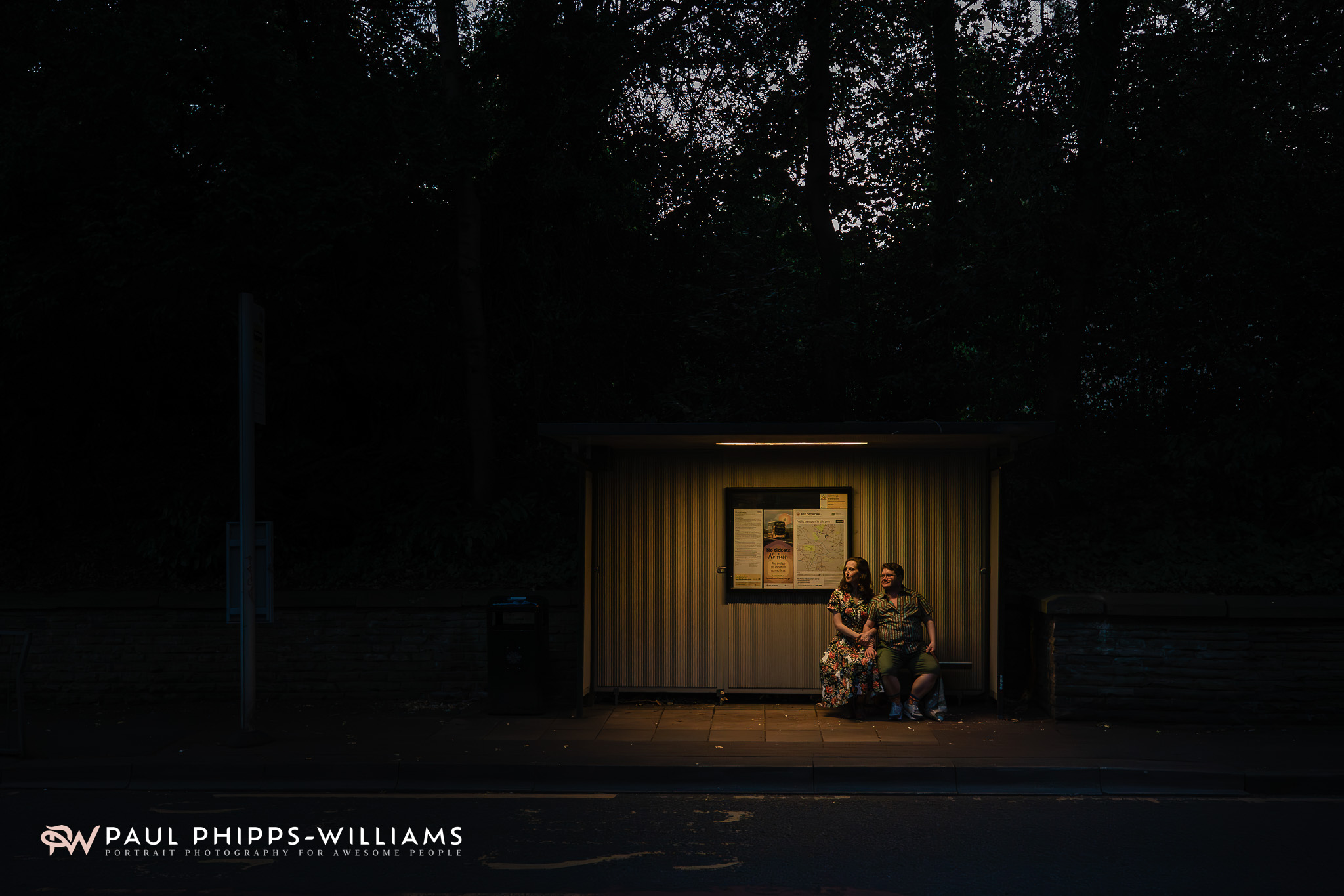 Frio and Georgia in a pool of light at a bus stop in Manchester in the evening