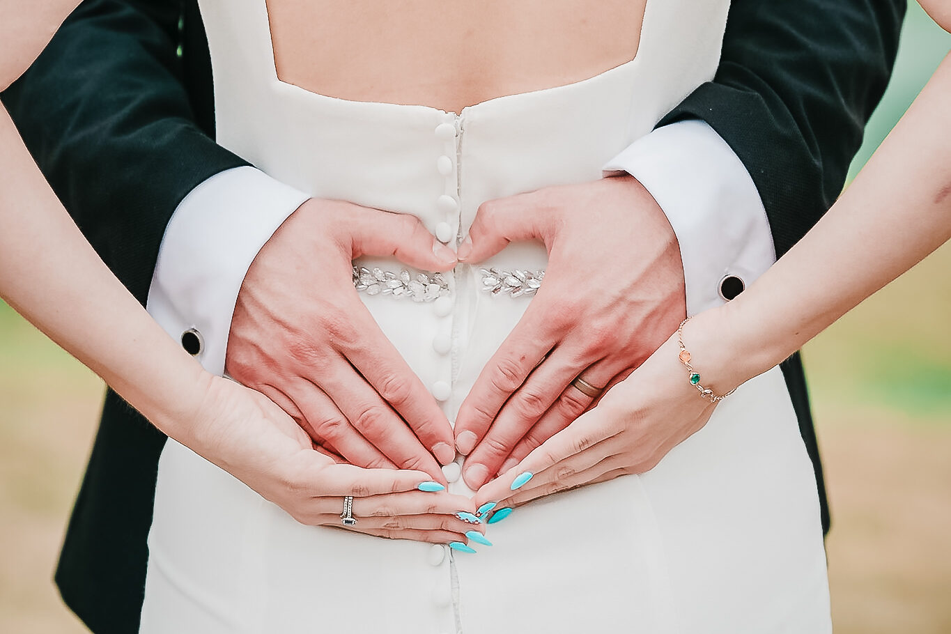 A grown makes a love heart behind his bride's back using his thumbs and forefingers