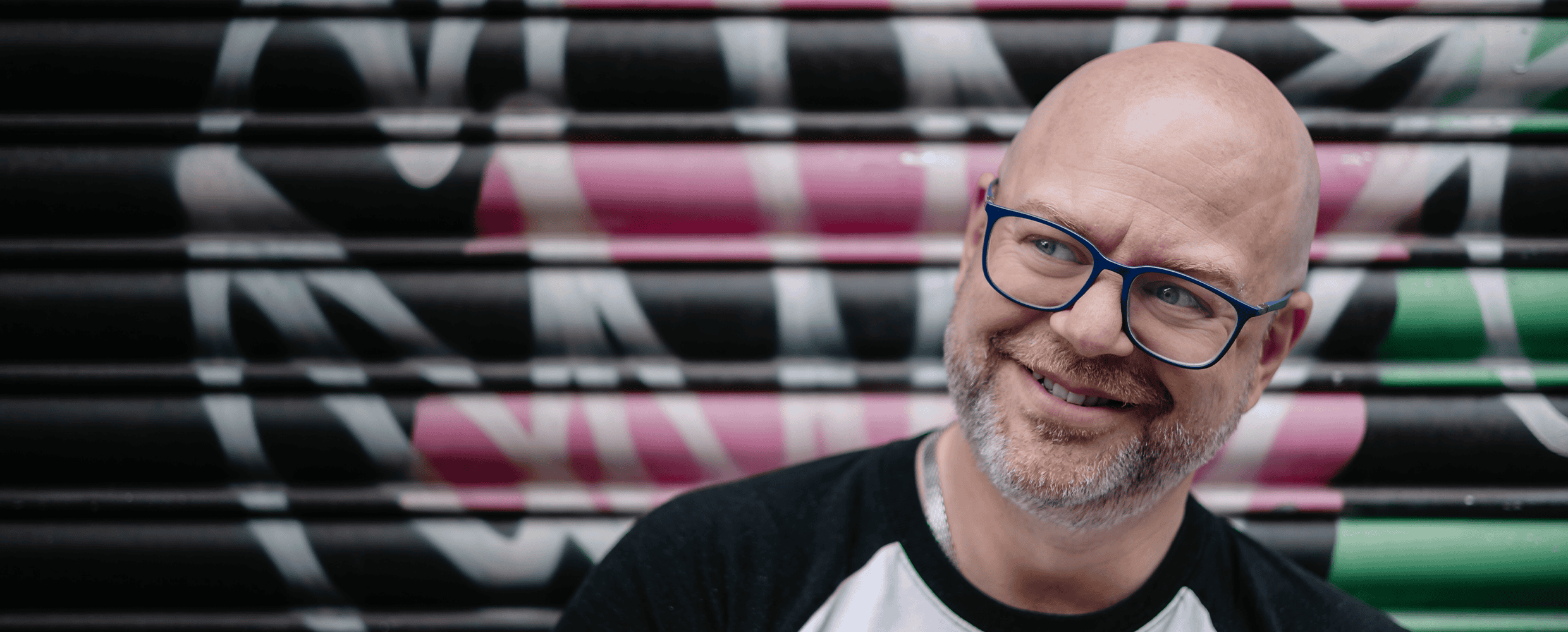Portrait of birmingham wedding photographer Paul Phipps-Williams with glasses against colourful graffiti background.