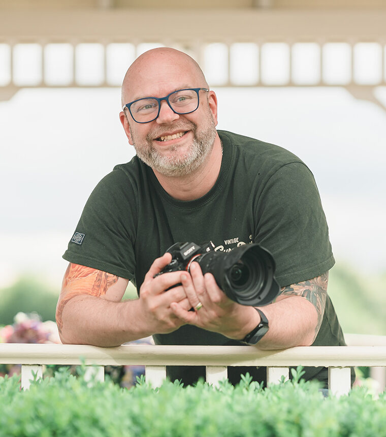 Photographer holding camera outdoors in a gazebo setting.