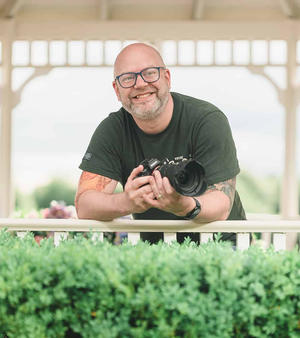 Photographer holding camera outdoors in a gazebo setting.