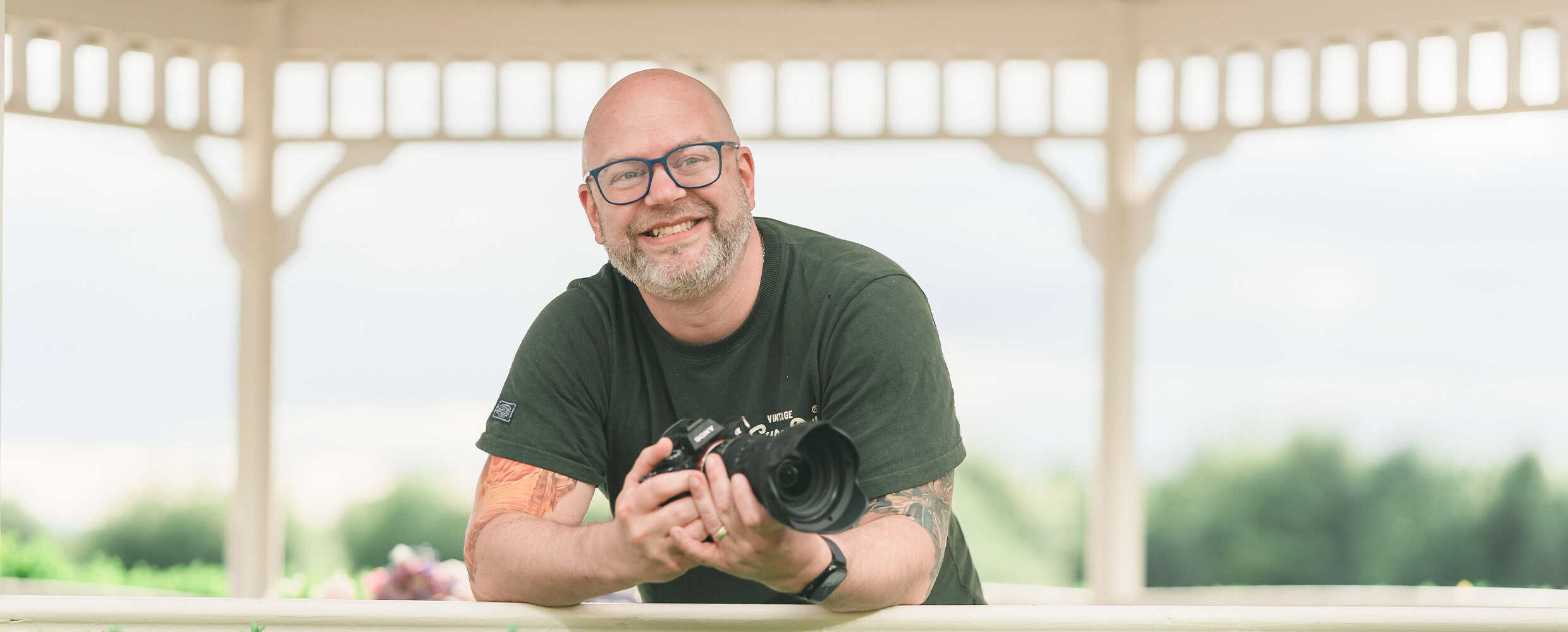 Photographer holding camera outdoors in a park setting.