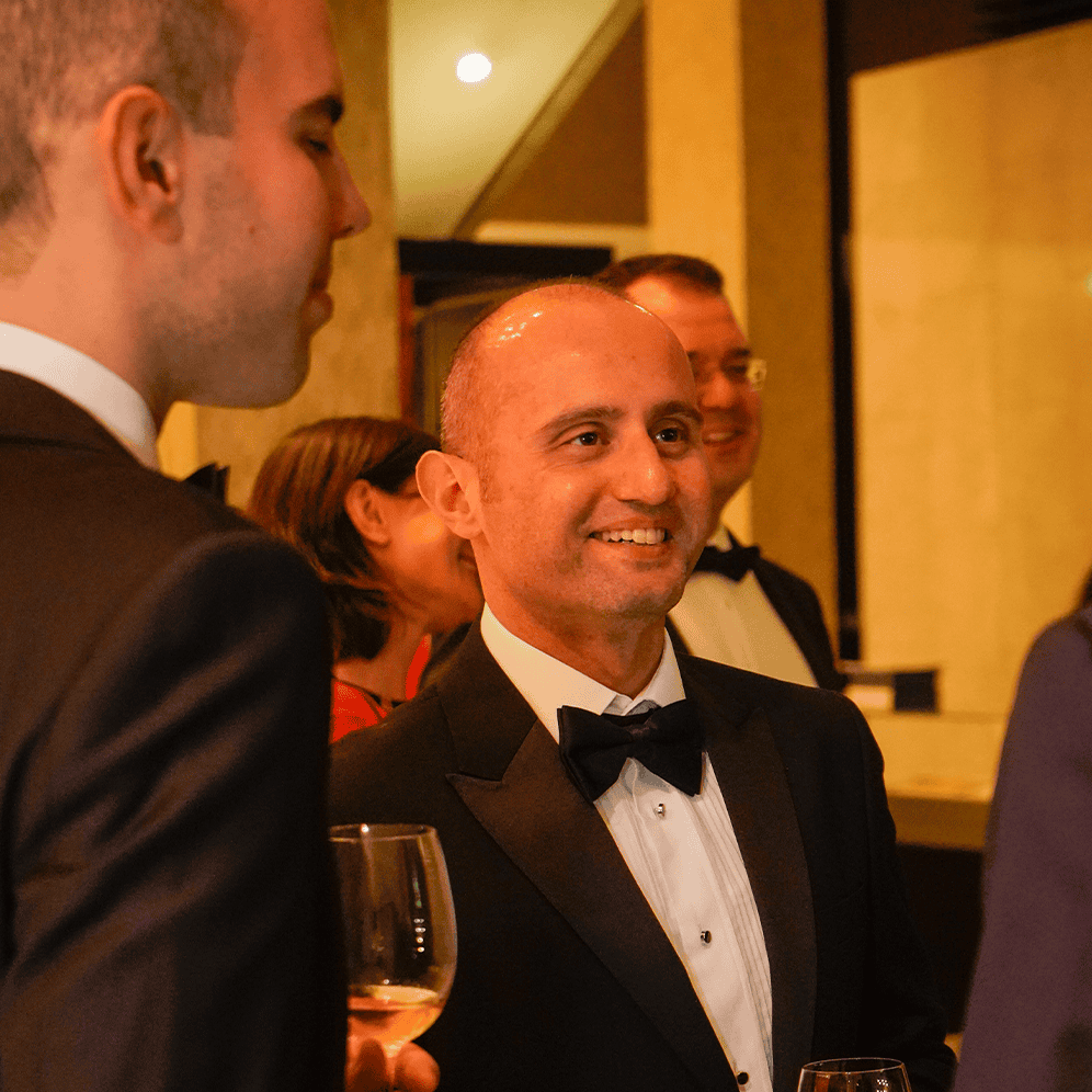 Tuxedo-clad men enjoying a formal social event, smiling and engaging in conversation.