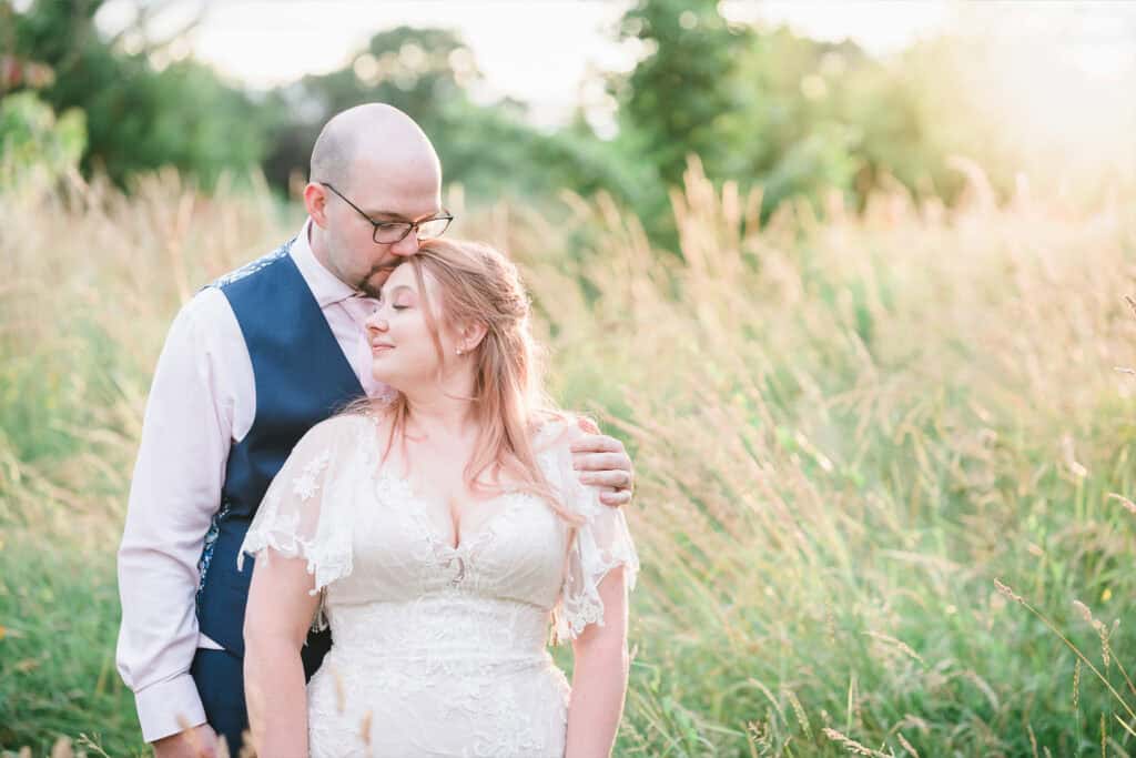 Romantic wedding portrait of a couple in a field during sunset, capturing love and intimacy.
