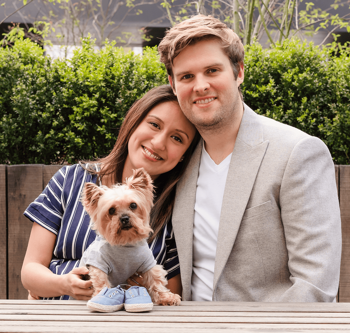 Family portrait with a woman, man, and small dog outdoors in a garden setting.