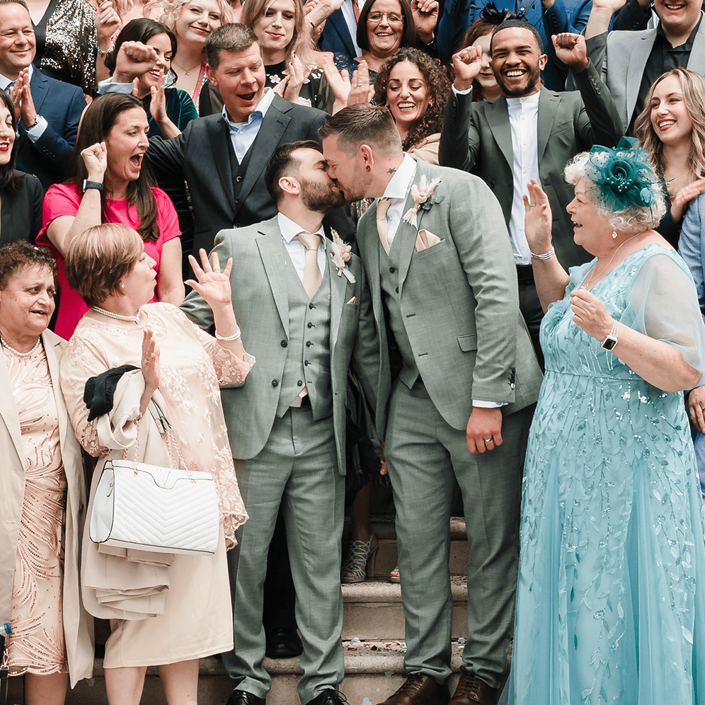 Wedding celebration, diverse guests, joyful atmosphere, two grooms kissing.
