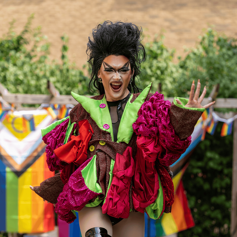 Colourful drag performer with bold makeup and elaborate outfit at outdoor event.