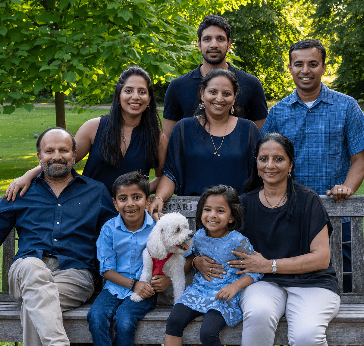 Family portrait in a lush park with children, adults, and a dog, capturing joyful moments outdoors.