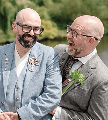 Men in formal suits smiling and laughing during an outdoor event.