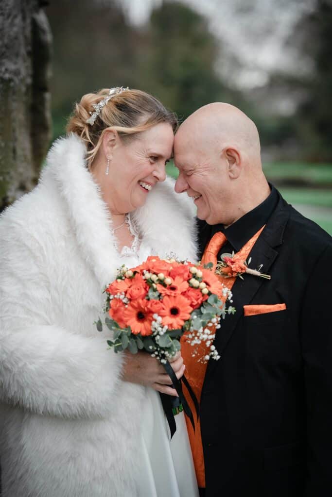 Wedding couple smiling and holding a bouquet in a scenic outdoor setting.