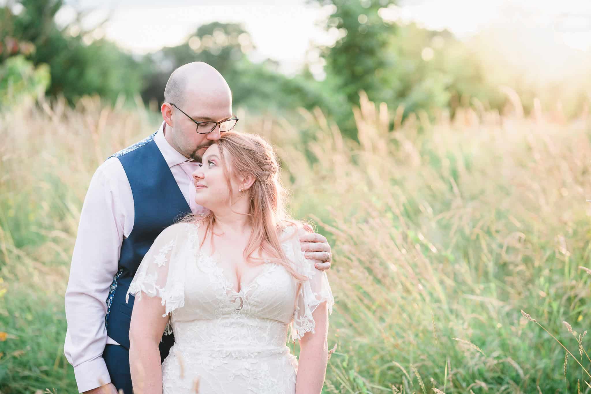 a bride and groom kiss in a field on their wedding day