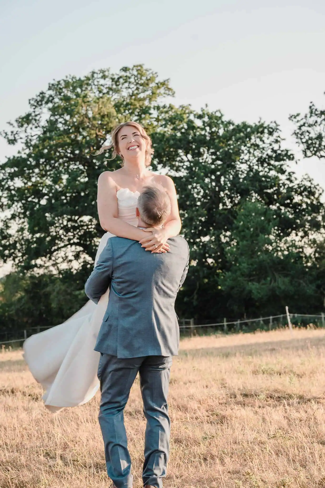 a groom lifts his bride in the air in a field at Newlands-Bishop-Farm