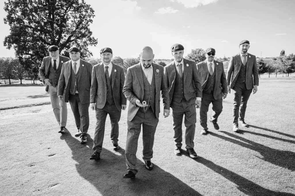 a peaky blinders wedding photo at windmill village coventry as groomsmen in flat caps flank a groom looking at his watch